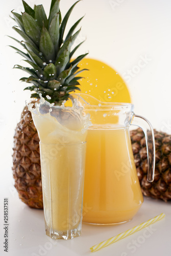 Jug and glass of pineapple juice with fruits on white background. Splash yellow drink. 