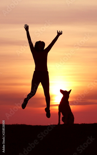 Girl and dog at sunset, Belgian Shepherd Malinois breed, incredible sunset, athletic girl jumping, the dog looks at the jumping girl