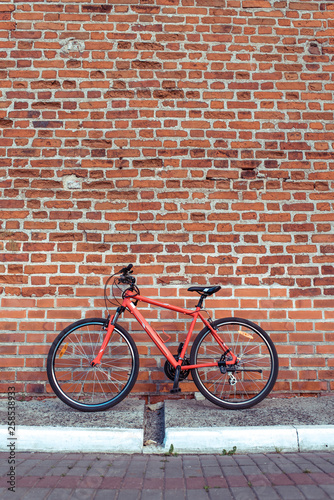 A red bicycle in summer in the city stands parked against a brick old wall. Free space for text. The concept of parking, walking, repair, bike wheels and a frame with a wheel.