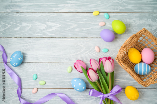 Easter holiday background with easter eggs in basket and tulip flowers on wooden table.