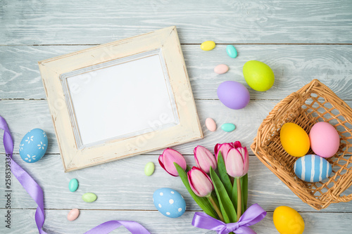 Canvas Print Easter holiday background with easter eggs in basket, photo frame and tulip flowers on wooden table