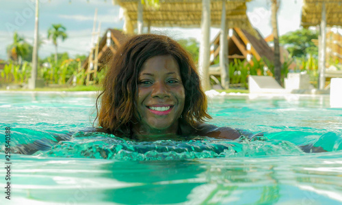 happy and beautiful black afro American woman in bikini having fun at tropical beach resort swimming pool relaxed and playful smiling cheerful enjoying luxury holidays