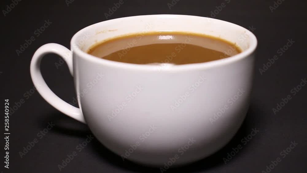 A teaspoon mix bleached coffee in a white cup. Black background.