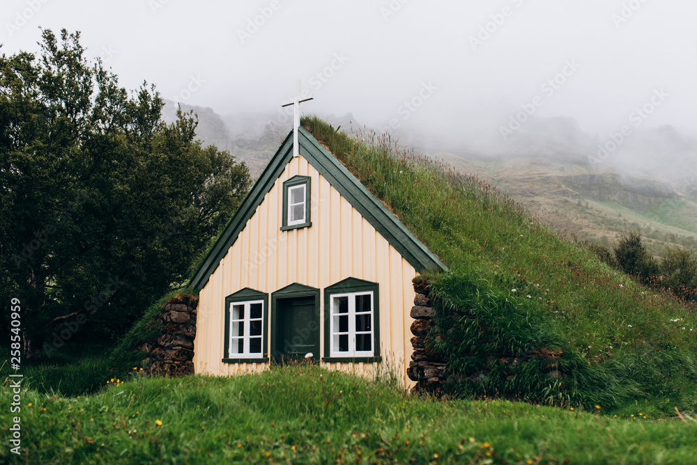 Wooden church with a green roof against the background of the mountains. Church in Iceland