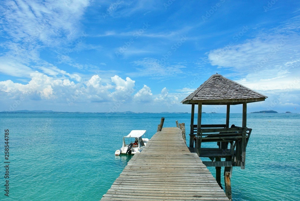 The wooden bridge stretches out to the middle of the sea with a view of the sky, and there is a white boat landing at Koh Samet Thailand. The wooden bridge stretches out to the middle of the sea with a view of the sky, and there is a white boat landing at Koh Samet Thailand.