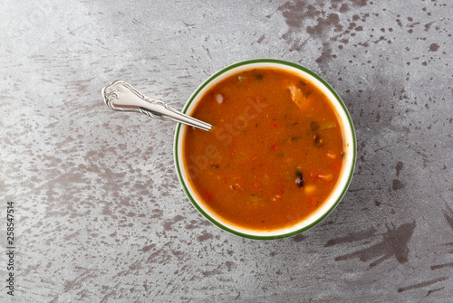 Top view of a bowl of chicken tortilla soup with a spoon on a gray background.