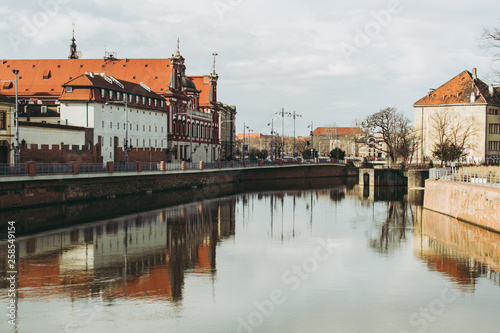 Cityscape of Wroclaw on a sunny spring day. Water of Odra river reflecting gray-blue sky and old classical buildings with red roofs. 