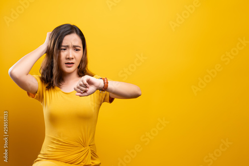 Shocked woman holding hand with wrist watch isolated on a yellow background