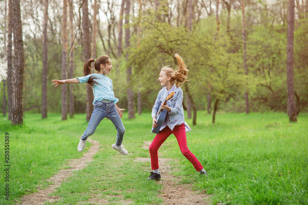 happy young rock band of two jumping and playing guitar little caucasian girls in green outdoor spring park during rehearsal happy young rock band of two jumping and playing guitar little caucasian girls in green outdoor spring park during rehearsal
