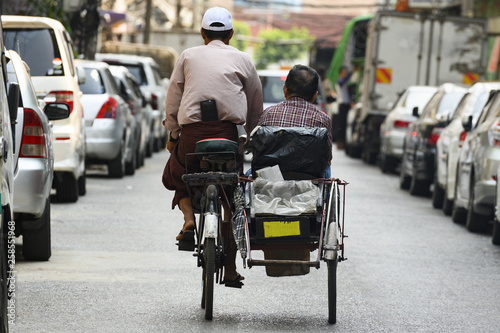 A unidentified Sai Kaa driver is carrying a passenger on his side car among the narrow streets of Yangon, Myanmar. The Sai Kaa rickshaw is a type of tricycle used in southeast Asia. photo