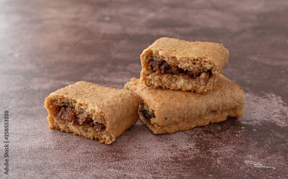 Side view of a blueberry fig bar broken in half on a whole bar atop a maroon background. Side view of a blueberry fig bar broken in half on a whole bar atop a maroon background.
