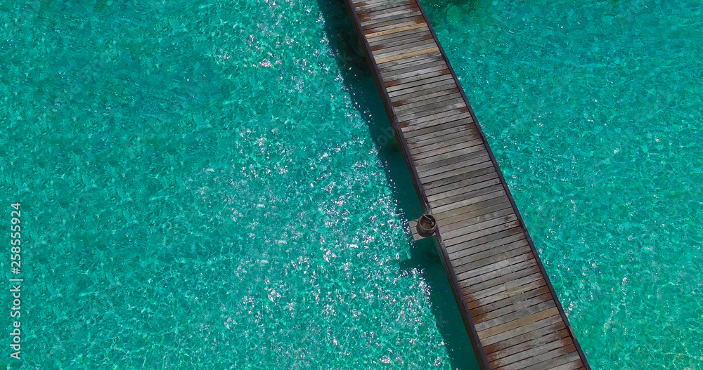 Aerial view from above of endless isolated wooden bridge above crystal clear turquoise water in Maldives, Maldivian paradise island