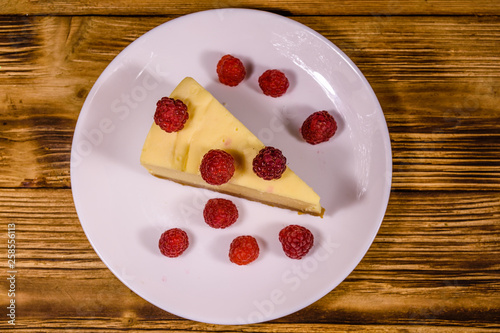 White plate with cheesecake New York and raspberries on wooden table. Top view