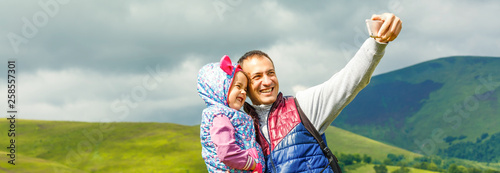 father with little daughter making selfie while hiking in summer mountains
