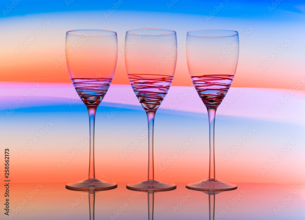 Three empty wine glasses in a row with colorful light painting behind