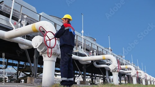 worker closes ball valve on cooling installations at gas compressor station, against background of blue sky