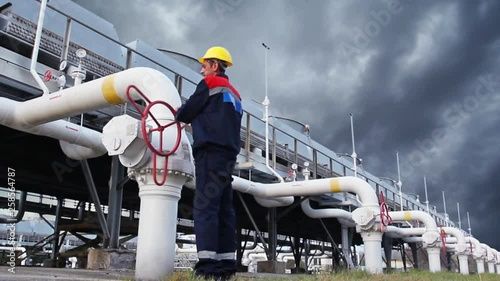 worker closes ball valve on cooling installations at gas compressor station, against background of thunderstorm sky