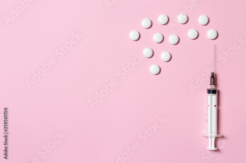 Syringe with white tablets as a injection and vaccination metaphor on pink background, flat lay, copy space