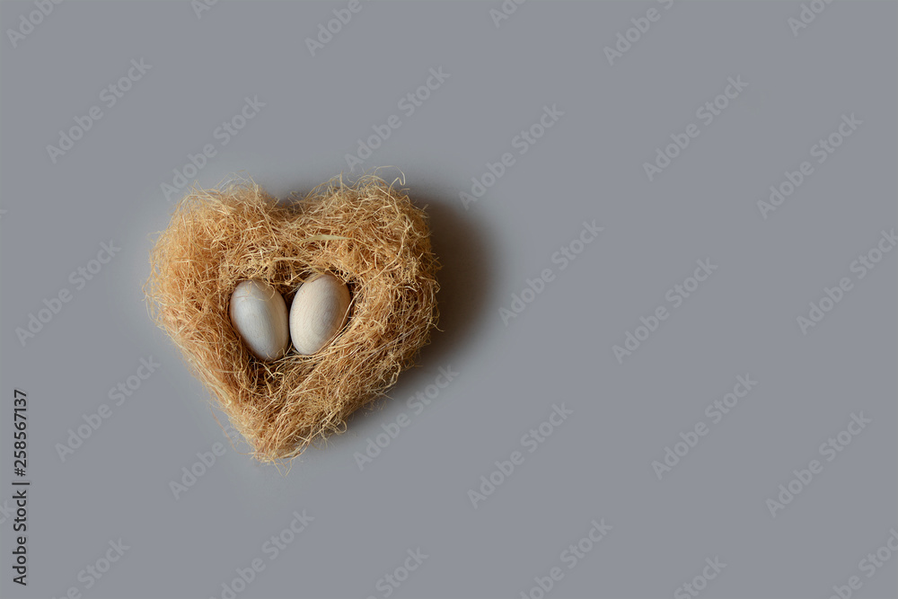 Two wooden easter eggs in a nest in the shape of a heart on a gray background. Easter greeting card for the wood industry. Two wooden easter eggs in a nest in the shape of a heart on a gray background. Easter greeting card for the wood industry.
