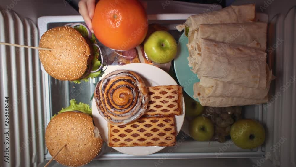 Top view on the shelf of the refrigerator, someone chooses between fruit and pastries and takes shawarma. Irregular nutrition and sleep disturbance. Top view on the shelf of the refrigerator, someone chooses between fruit and pastries and takes shawarma. Irregular nutrition and sleep disturbance.