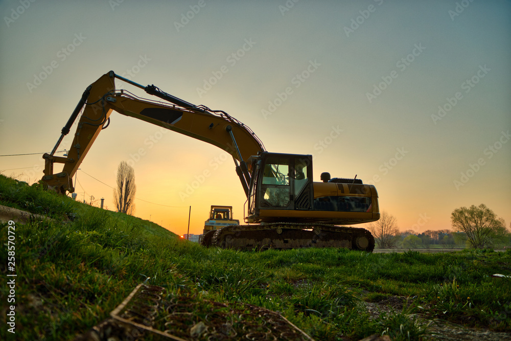 Excavator at sunrise by the river bank Excavator at sunrise by the river bank