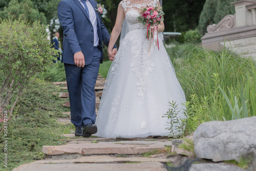 bride and groom walk together by the hand in the park bride and groom walk together by the hand in the park