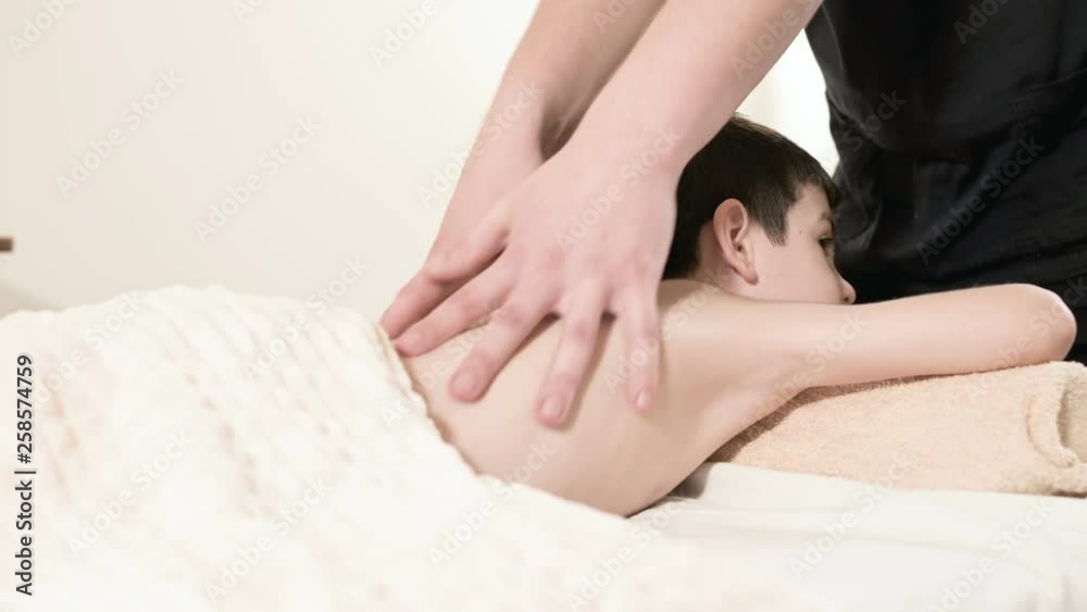 A male physiotherapist masseur makes a healing relaxing massage to a little smiling boy lying on a massage bed. Massage of the loin and back