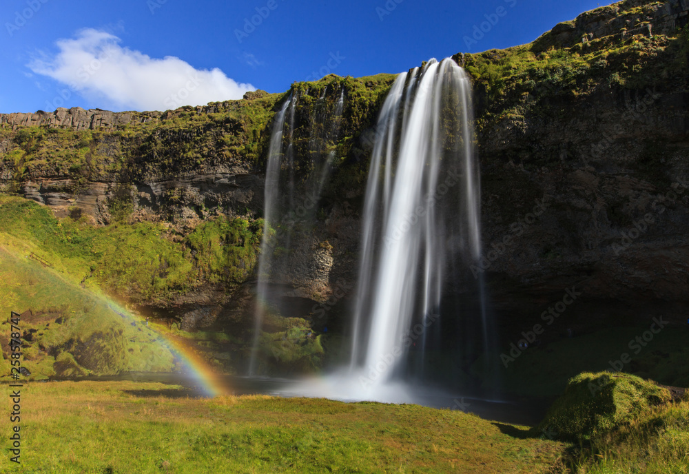 Wonderful view of Seljalandsfoss Waterfall in Iceland. Sunlight day in summer with rainbow and green landscape. Famous landmark on the route number one.