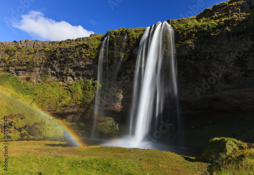Wonderful view of Seljalandsfoss Waterfall in Iceland. Sunlight day in summer with rainbow and green landscape. Famous landmark on the route number one.