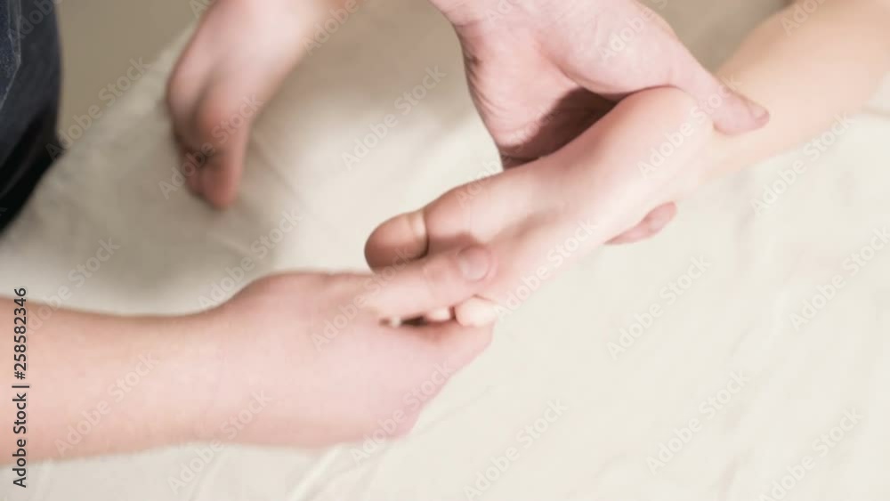 Close-up Male physiotherapist masseur doing a healing relaxing foot massage to a small child lying on a massage bed Close-up Male physiotherapist masseur doing a healing relaxing foot massage to a small child lying on a massage bed