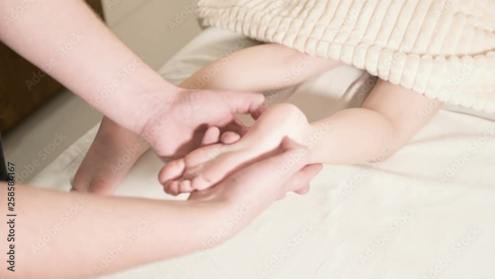Close-up Male physiotherapist masseur doing a healing relaxing foot massage to a small child lying on a massage bed Close-up Male physiotherapist masseur doing a healing relaxing foot massage to a small child lying on a massage bed