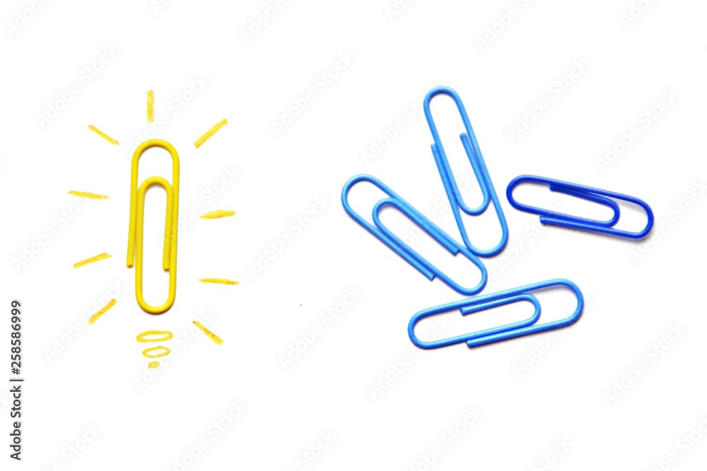 Obraz premium A yellow paper clip as a symbol of a light bulb that radiates lies on a white surface and symbolized the brainstorming - next to it are other paper clips without illusion