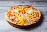 Fresh pizza on wooden stand on the table. Tasty pizza with tomato and cheese on the wooden background. Close-up