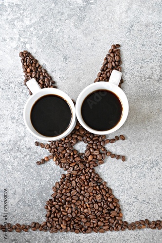 With fresh coffee beans and two cups of freshly brewed black coffee, a hare is shaped on a bright marble surface - concept with coffee beans as a gift for Easter - with room for text or other elements