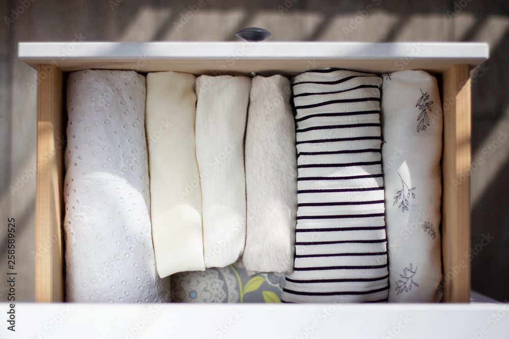 white lightweight women's clothing neatly folded in a vertical row in a chest drawer in sunlight