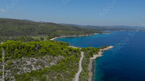 Aerial drone view of blue sea surface surrounded with trees. Top view of dark blue ocean water surface, seashore, forest, car road.