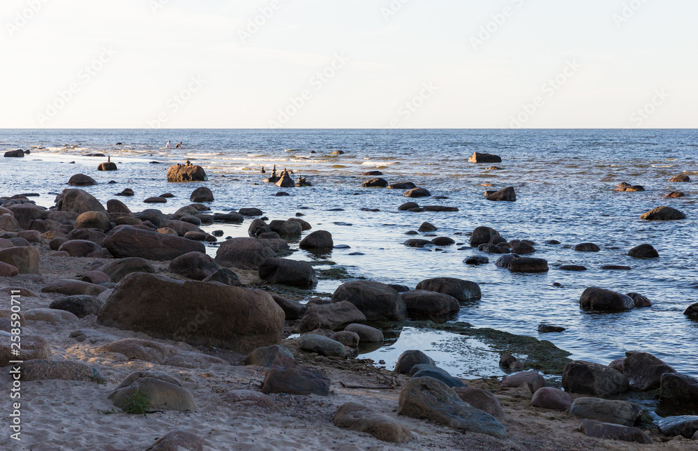 many large stones on the sandy sea shore and also in the water, small stones have been stacked on several stones; sea view with horizon many large stones on the sandy sea shore and also in the water, small stones have been stacked on several stones; sea view with horizon