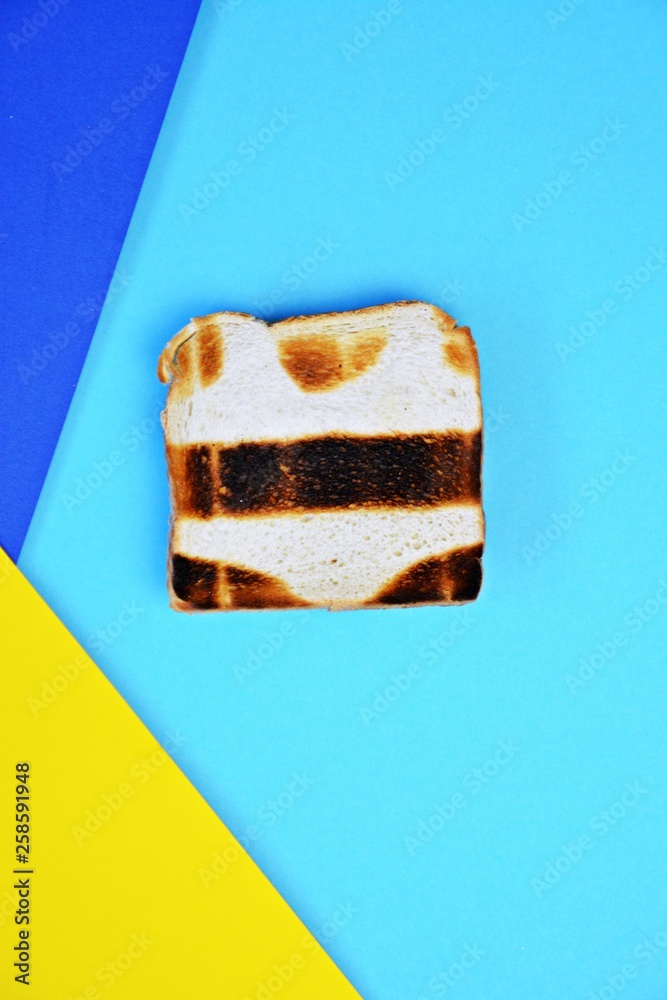 Abstract Toast A toast lies on a colored surface. The toast is not toasted everywhere ...