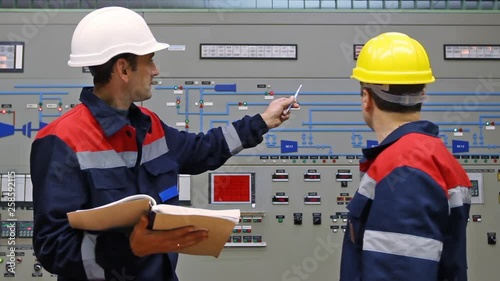 two engineers talk while looking into logs and giving explanation about circuit at main control panel of gas compressor station, closeup