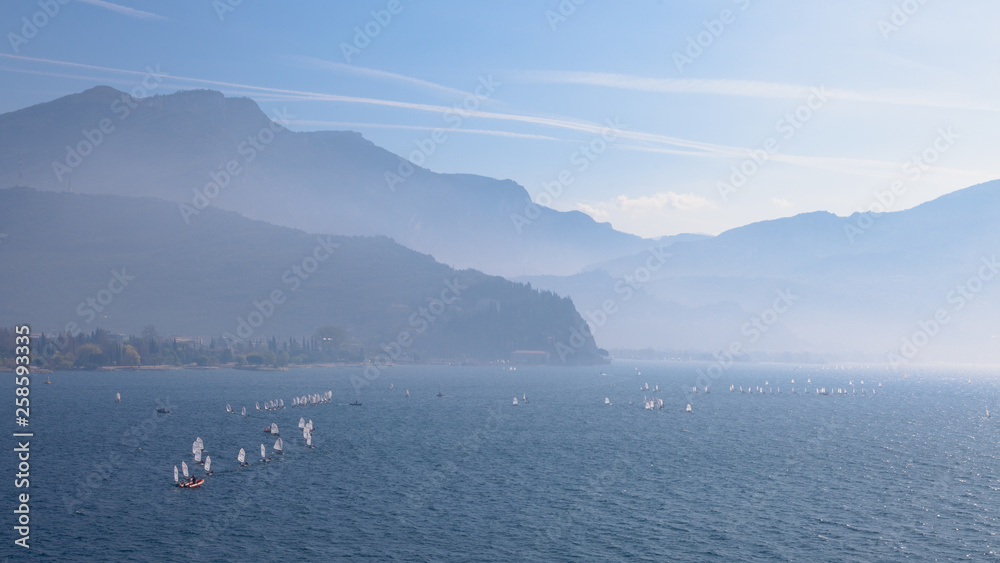 Yachting. Landscape panorama with yacht sailer ship sailing by lake or sea waves in evening sunset sun sunbeams. Fishing sporting poat on water. Mountains background. Garda Lake, Veneto region, Italy