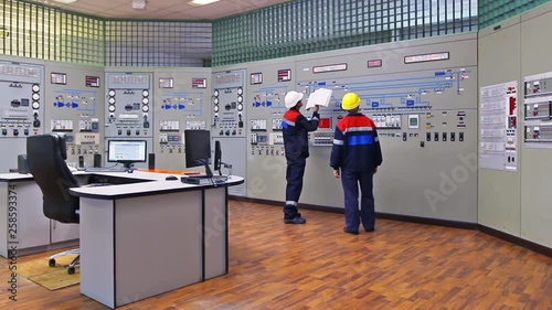 two engineers talk while showing examples on circuit at main control panel of gas compressor station