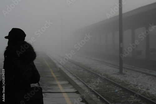  Silhouette of a woman at the railway station in dense fog. Rails leaving the distance. Mood. Expectation. Free space for text.