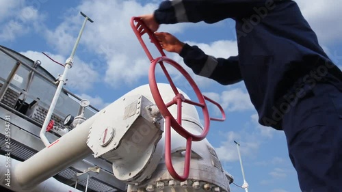 worker opens ball valve on cooling installations at gas compressor station, against background of cloudy sky, closeup 