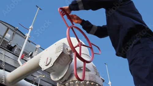 worker opens ball valve on cooling installations at gas compressor station, against background of blue sky, closeup
