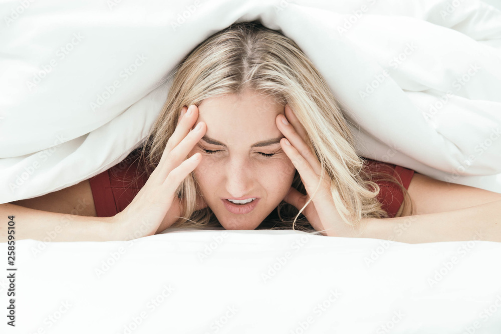 Fototapeta premium Grumpy blonde girl under white covers