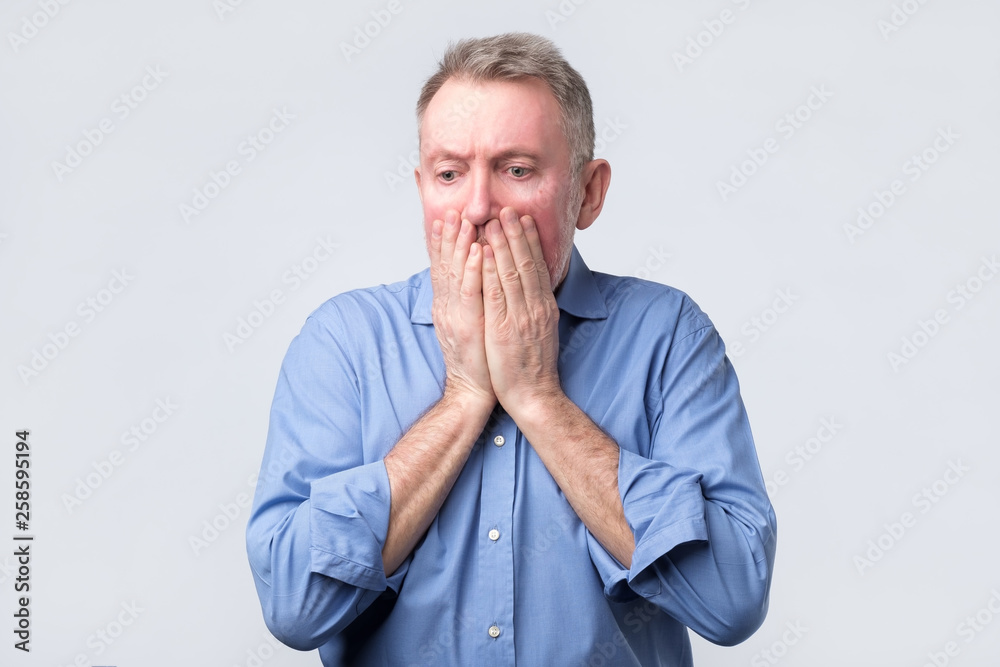Senior man covers mouth and looks desperately Senior man covers mouth and looks desperately