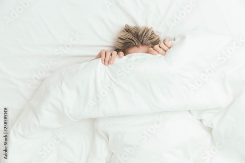 Happy Caucasian Blonde Girl Peeking from Under White Duvet Covers