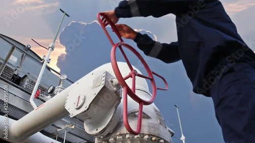 worker opens ball valve on cooling installations at gas compressor station, against background of sunset, closeup