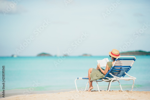 Young woman reading book on chaise-lounge on the beach