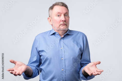 Obraz na płótnie Confused senior caucasian man in blue shirt is unsure in studio